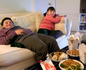 Overweight Brother and Sister Sitting on a Sofa Eating Takeaway Food and Watching the TV